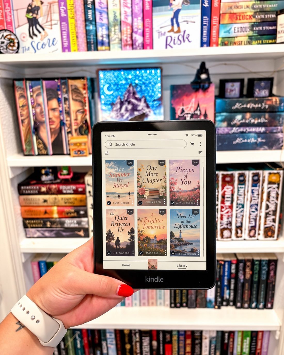 Hand holding a Kindle showing a library of published book covers in front of a full bookshelf